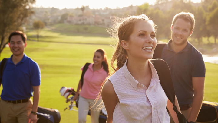 A group of people smiling with golf club bags over their shoulders on the gold course on a summer day