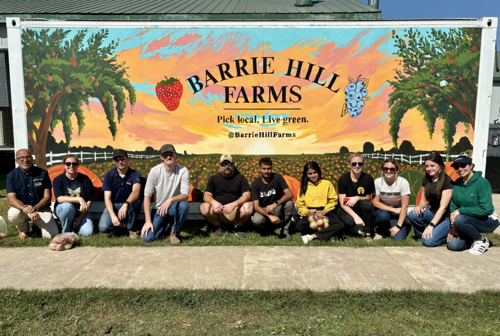 A group of people kneel in a row in front of a sign reading: Barrie Hill Farms.