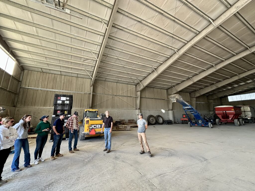 A group of people stand in a massive warehouse with agriculture machinery parked inside.