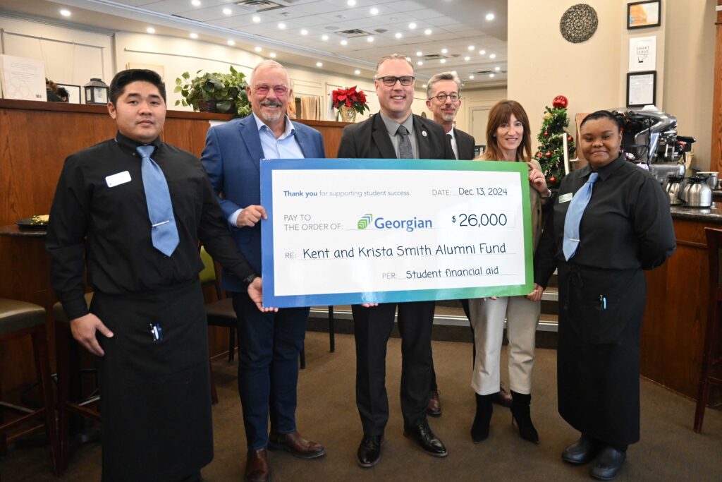 Six people stand in a restaurant and hold up an oversized cheque.