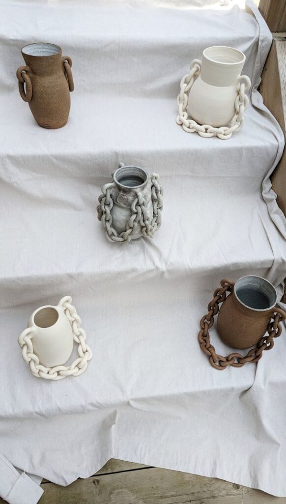 Five pieces of brown, grey and white ceramic pottery sit on a large white cloth draped over stairs.