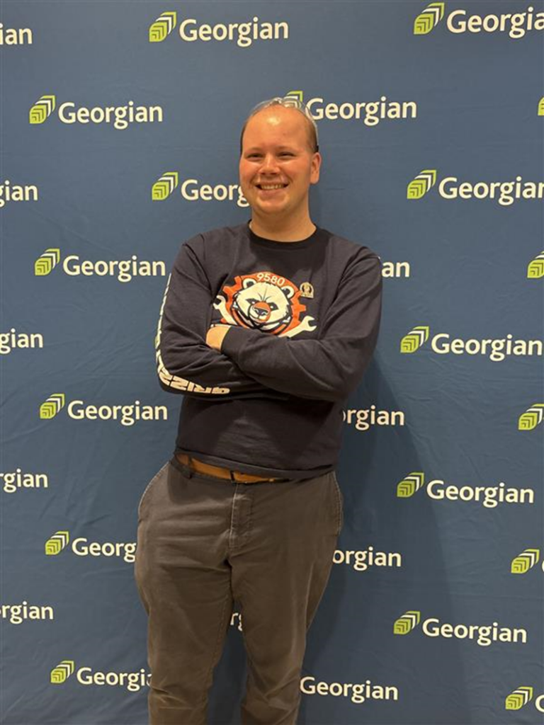 Person standing with arms crossed smiling in front of photo backdrop.