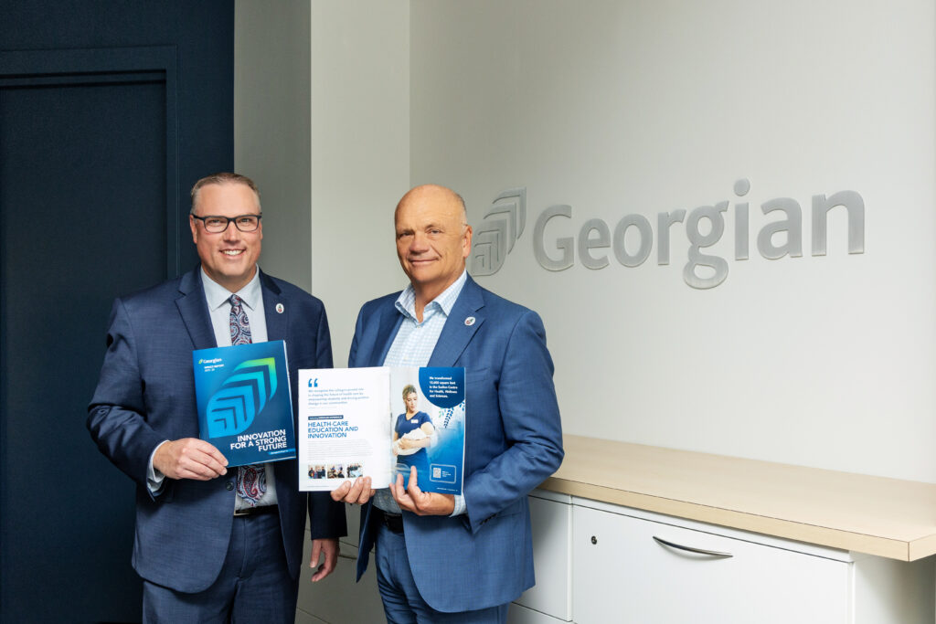 Two people wearing blue suits stand together and each hold up a book reading "Innovation for a Strong Future." 