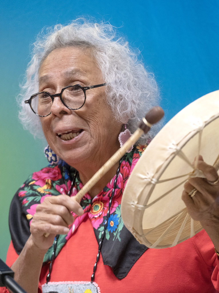 An older Indigenous woman (Shirley John) drumming.