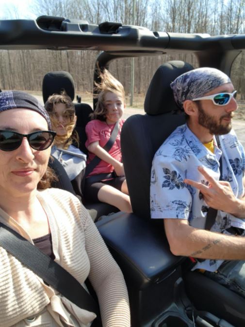 A selfie of two adults and two children in a vehicle.