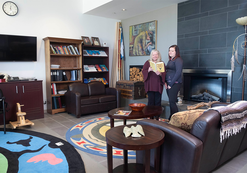 a female student and Indigenous student advisor reading a book in the Barrie Campus Indigenous Resource Centre