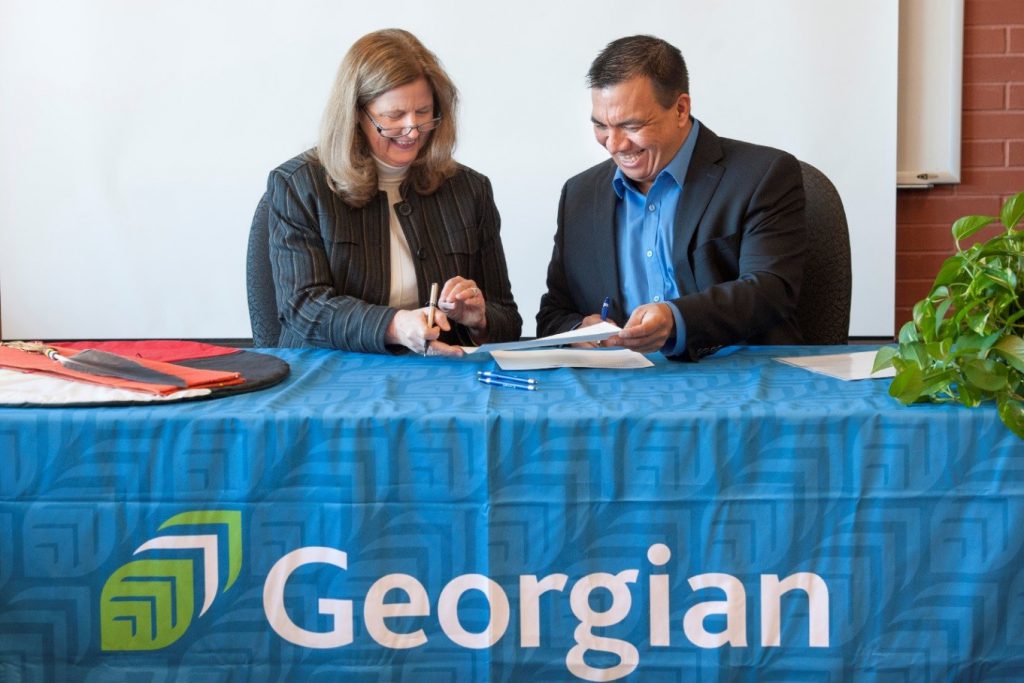 President and CEO MaryLynn West-Moynes and AETC Chair Kevin Wassegijig sitting at a table signing the Indigenous Education Protocol