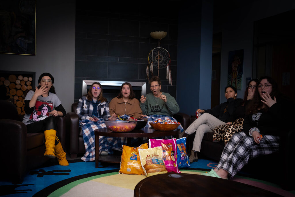 Seven people sit on several couches with bowls of snacks in front of them. 