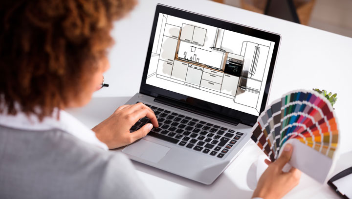 Kitchen and Bath Designer sitting at a desk using AutoCAD software on a laptop and colour swatches to design a kitchen remodel