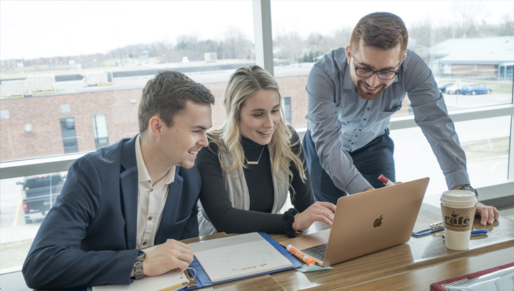 Two men and a woman collaborating together and looking at a laptop.