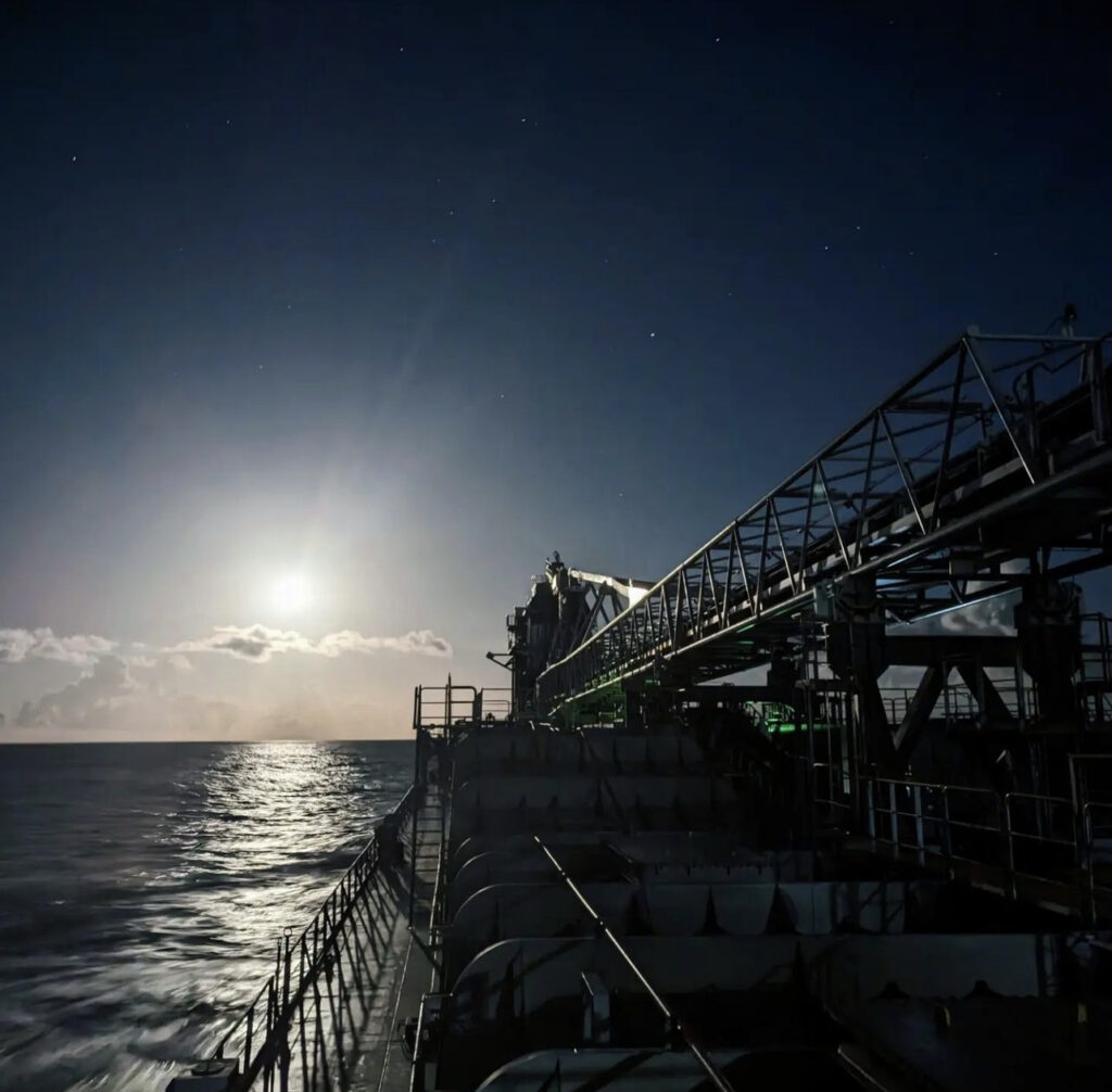 A ship sails across an ocean at nighttime.
