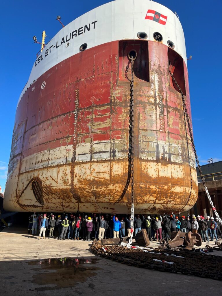 A group of people standing underneath a large red and white carrier ship.