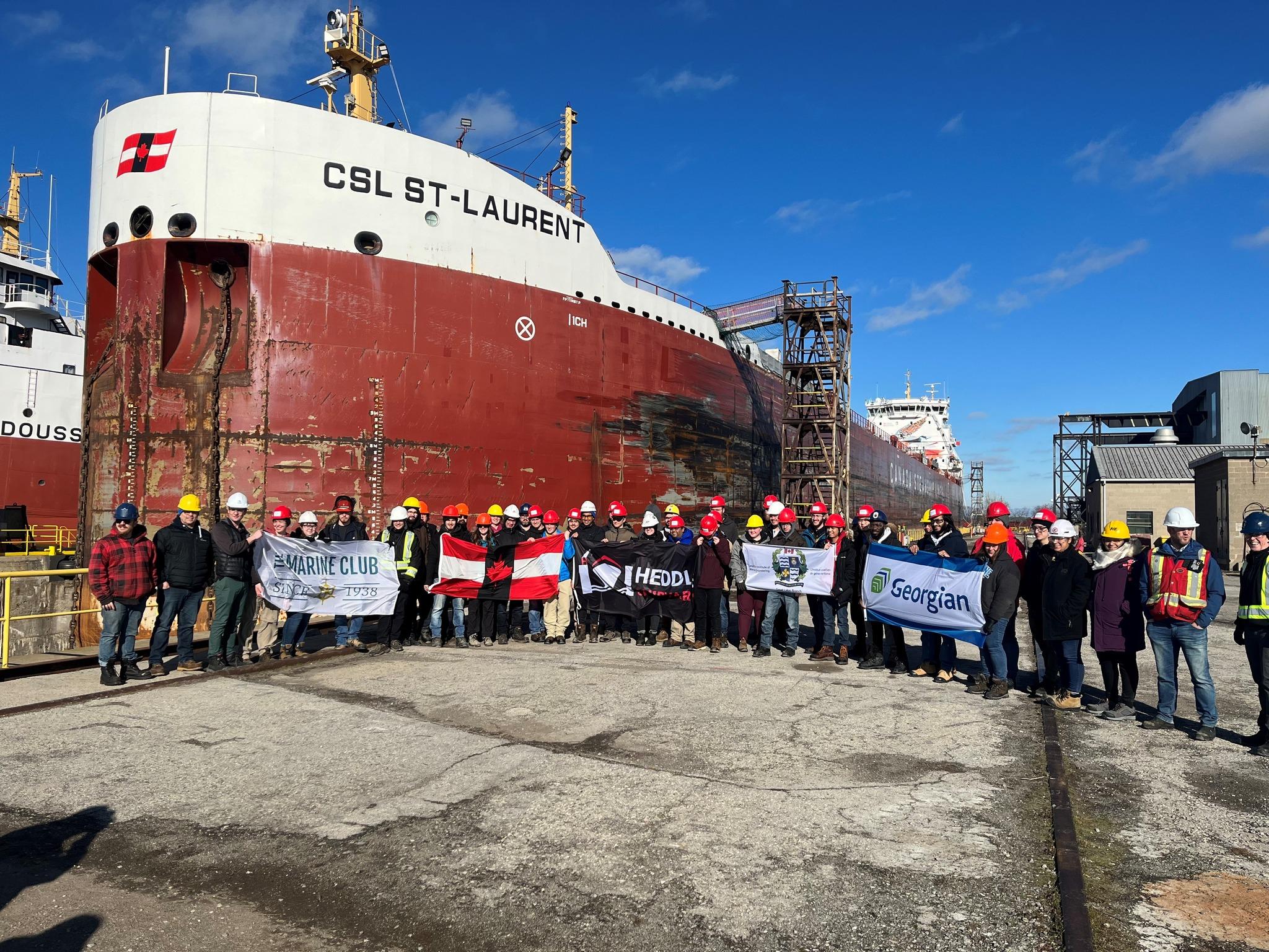 A group of people holding banners, standing outside in front of a red and white carrier ship.