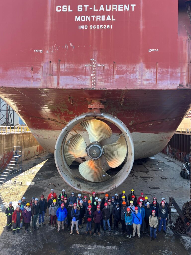 A group of people standing underneath a large red and white carrier ship.
