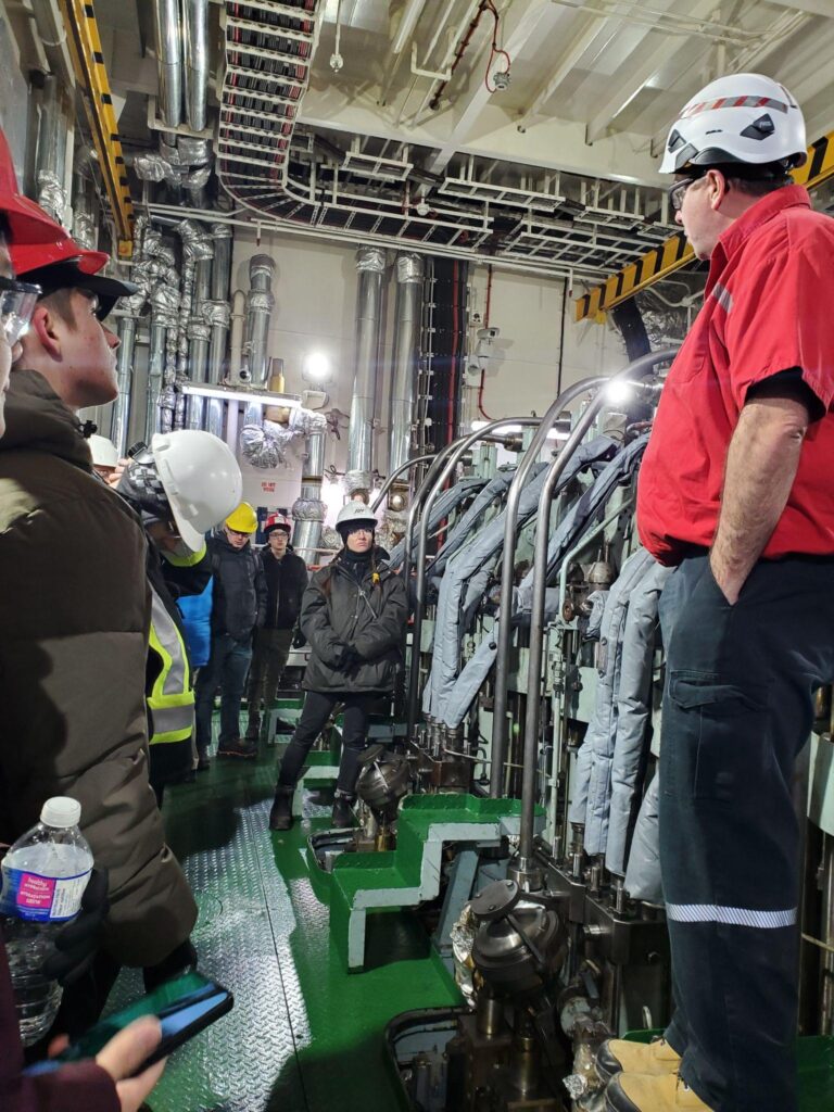 A group of people wearing hard hats, standing around pumps and control systems inside a ship.