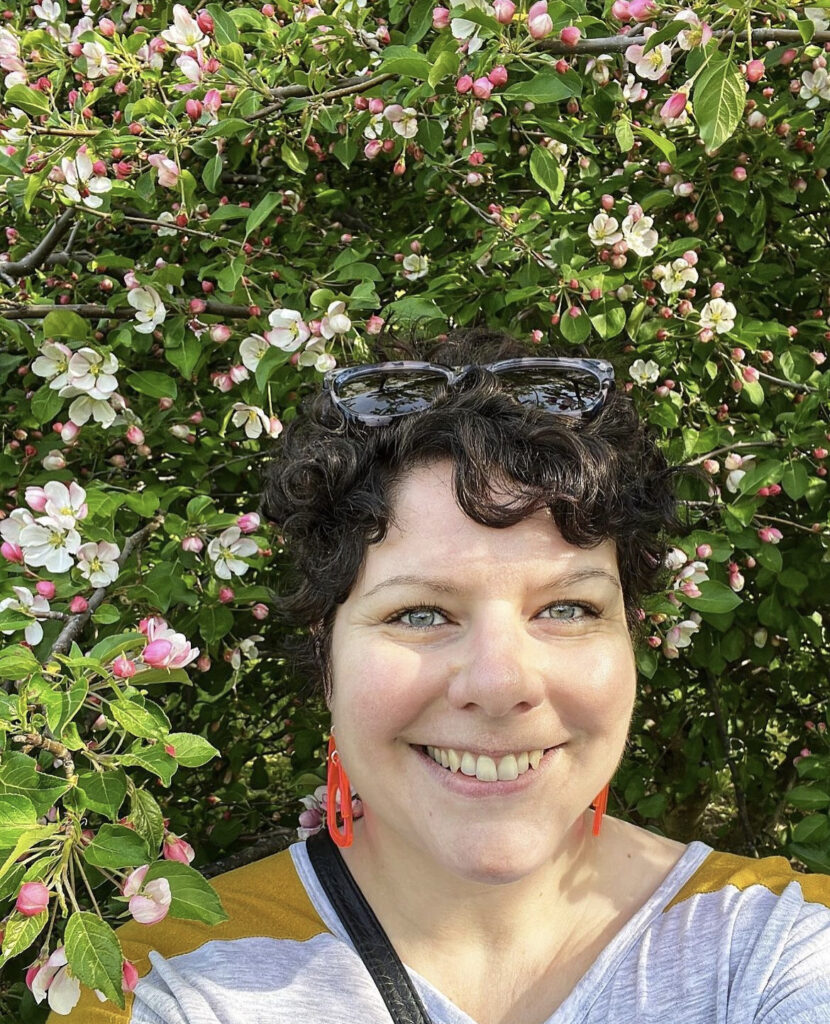 A person takes a selfie against a backdrop of a flowering tree.