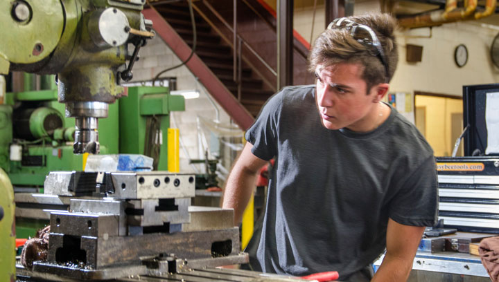 Person in a grey t-shirt with sunglasses on their head in a workshop using mechanical engineering equipment