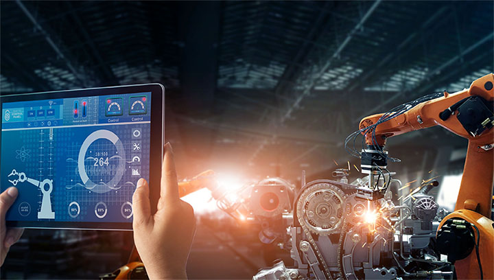 A mechntronics technician holding a tablet programming a robotic arm.