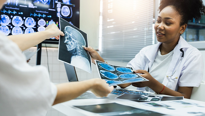 Person in a clinical setting reviews a head and neck X-ray film while another person points to an area of interest.