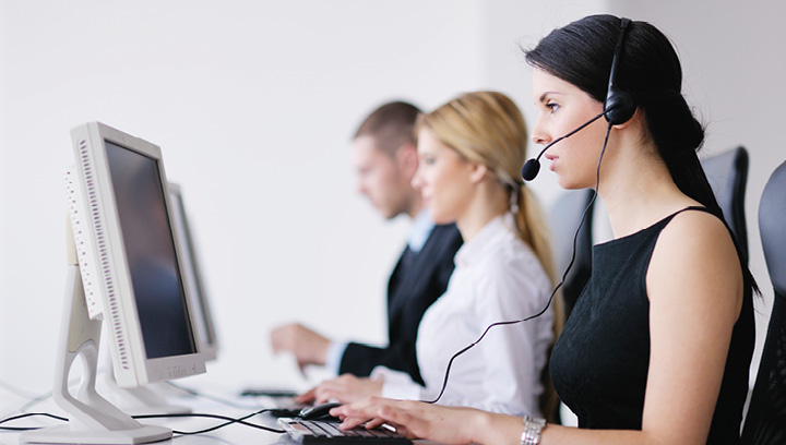 A medical transcriptionist with long, black hair, wearing a black tank top and a wired headset with microphone while entering information on a computer