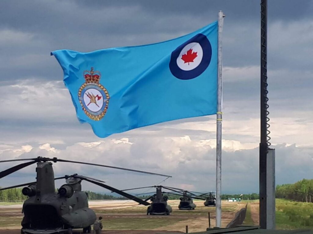 A line of Chinook helicopters sitting on the ground, with a blue air force flag in the foreground.