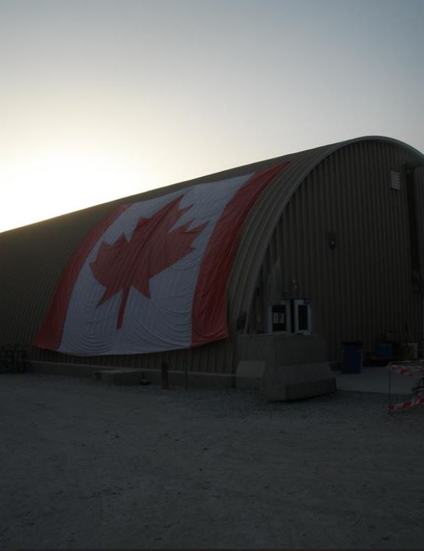 A long building with a curved roof has an oversized Canada flag draped over its side.