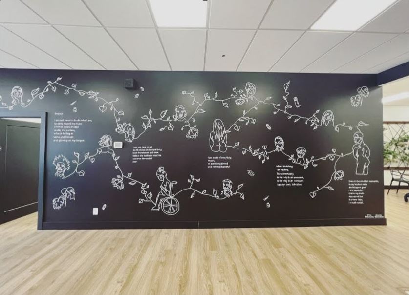 A black wall with white art of people connected by vines and flowers.