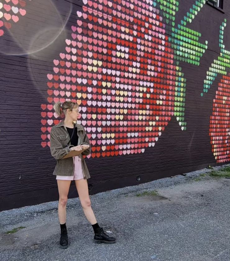 A person stands outside in front of a strawberry mural on a black wall.