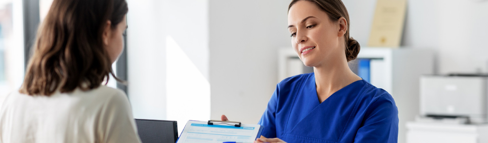Woman in scrubs showing another woman information on a clipboard