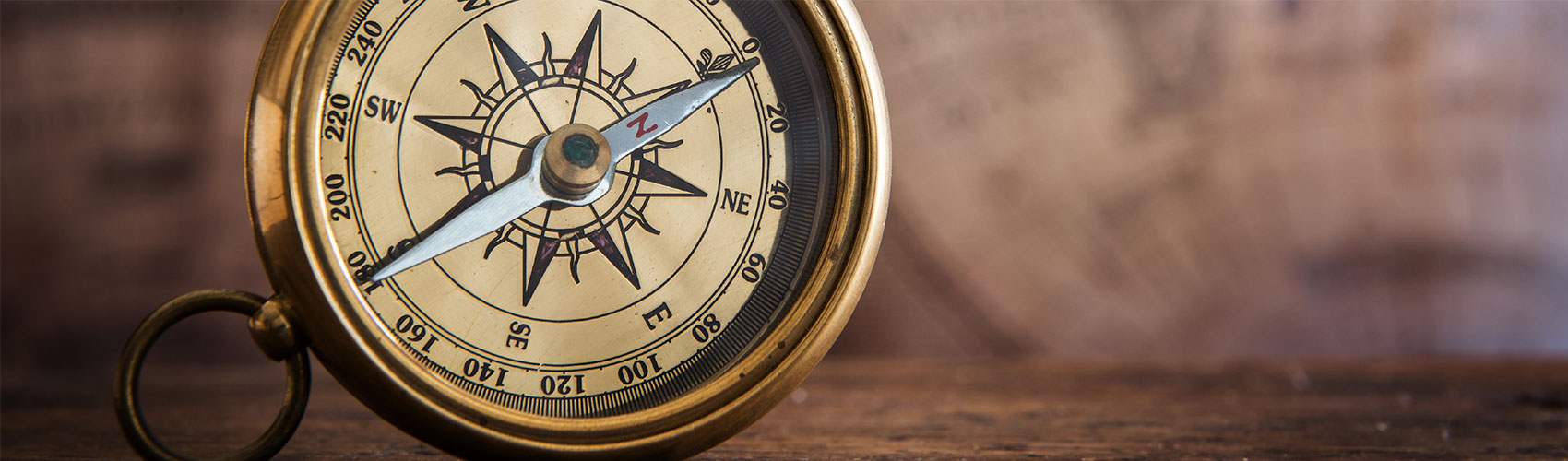 A round, gold compass resting on a wooden tabletop