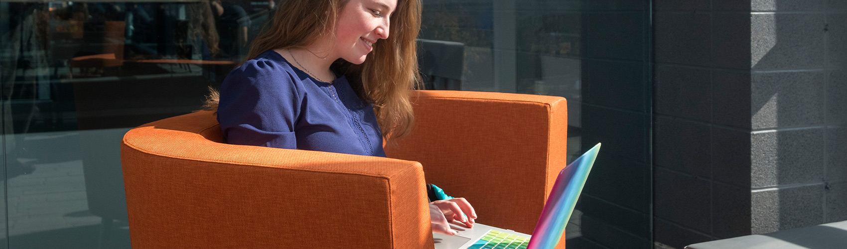 female student using a laptop and sitting in an orange lounge chair