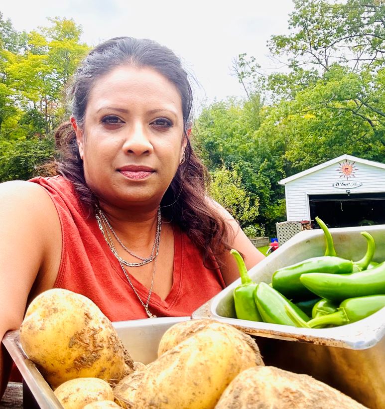 A person stands outside and holds up two containers of vegetables picked from a garden.