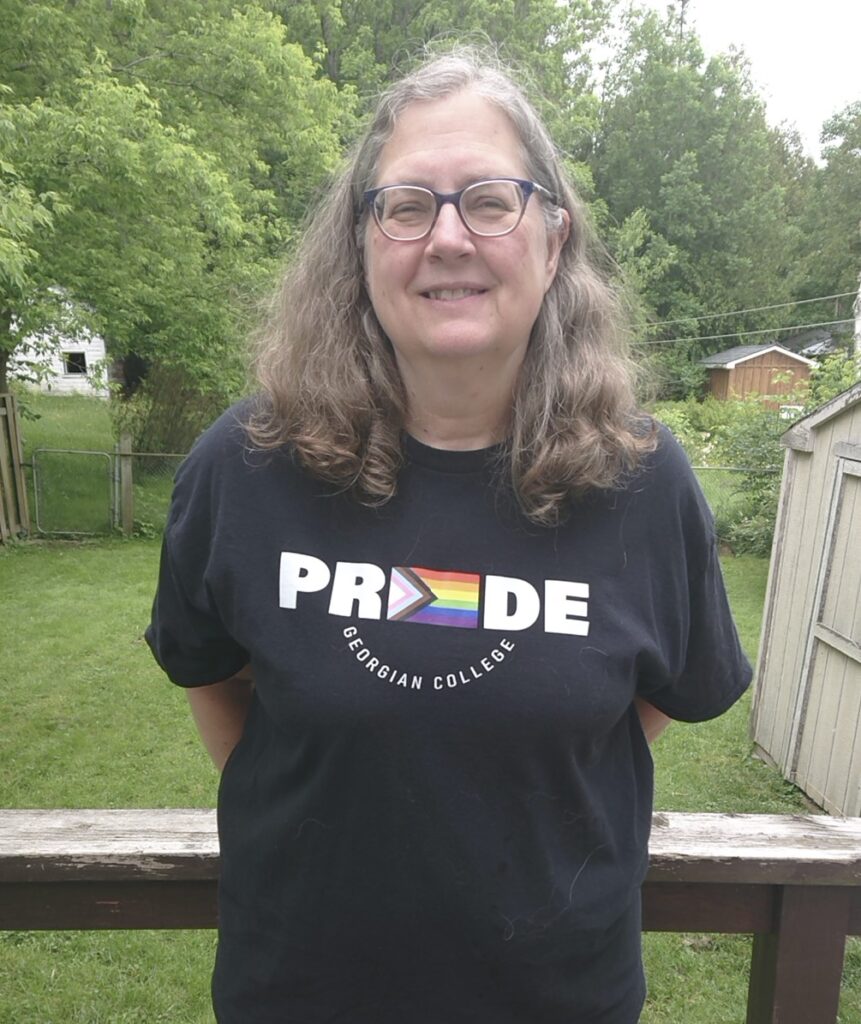 A person wearing a black shirt with text reading "Pride Georgian College" stands on a deck outside overlooking a backyard.