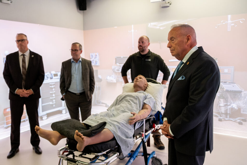 Four people stand around a simulator hospital patient lying on a gurney.