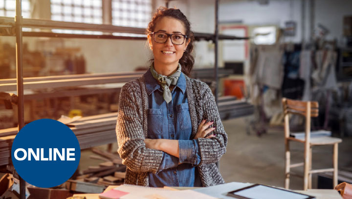 a person with brown hair and glasses standing in a workshop smiling with their arms