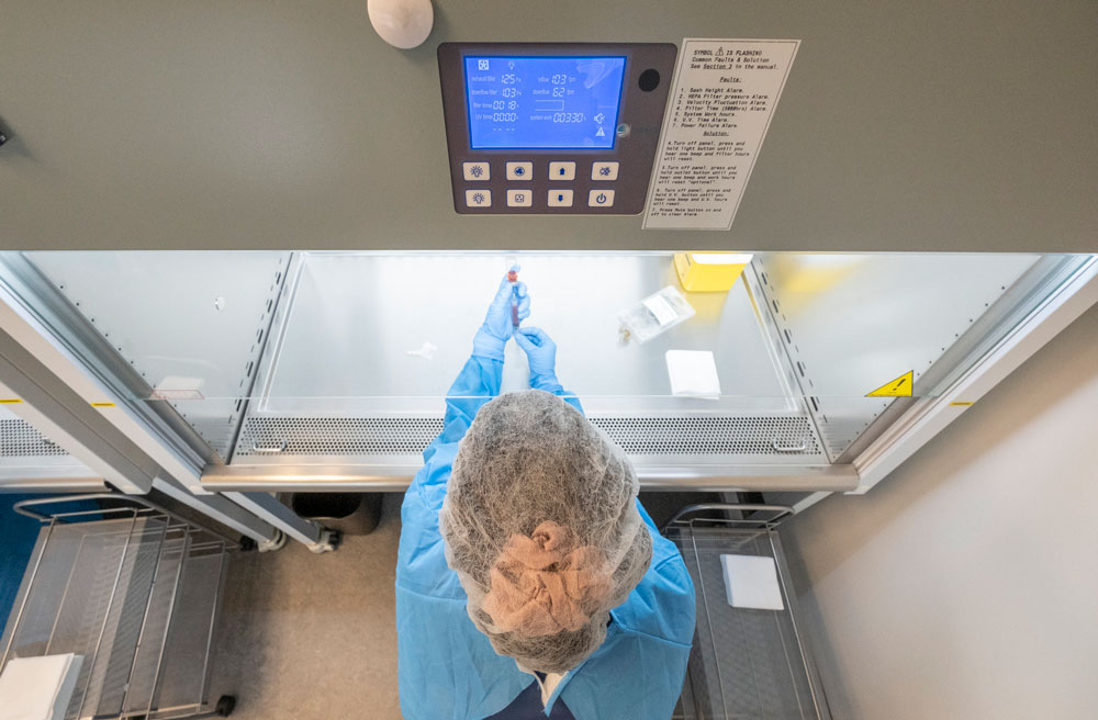 A Georgian College Pharmacy Technician student wearing blue scrubs, a face covering, gloves and hairnet preparing a syringe from a vaccination vial