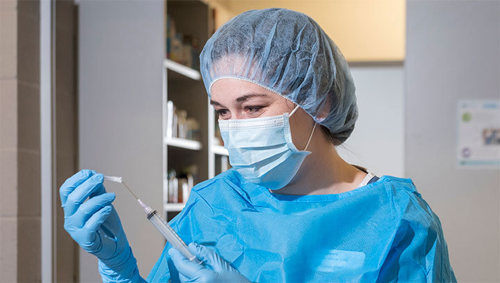 Georgian College Pharmacy Technician student wearing scrubs, a face covering and hair mask preparing a vaccination syringe