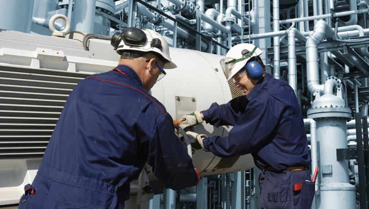 Two power engineering professionals wearing work jumpsuits and hard hats working on a piece of equipment