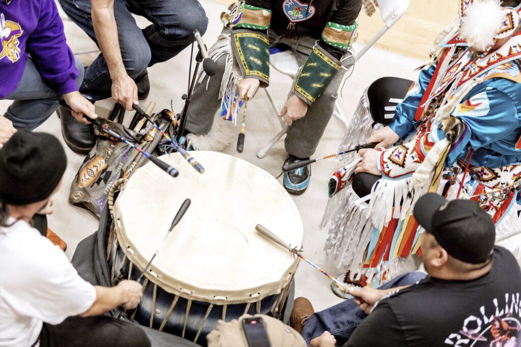 An aerial view of people sitting around a drum and drumming. 