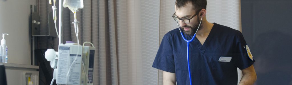 A Practical Nursing student at Georgian College wearing navy blue scrubs and wearing a stethoscope in the nursing simulation lab