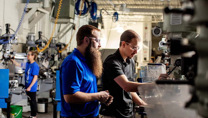 Two people wearing safety glasses working with industrial machinery in a workshop, focusing on precise technical tasks.