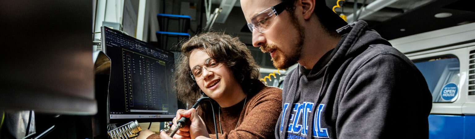 Two people wearing safety glasses working with industrial machinery in a workshop, focusing on precise technical tasks.