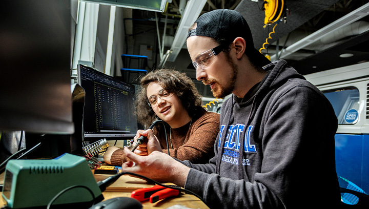 Two people wearing safety glasses working with industrial machinery in a workshop, focusing on precise technical tasks.