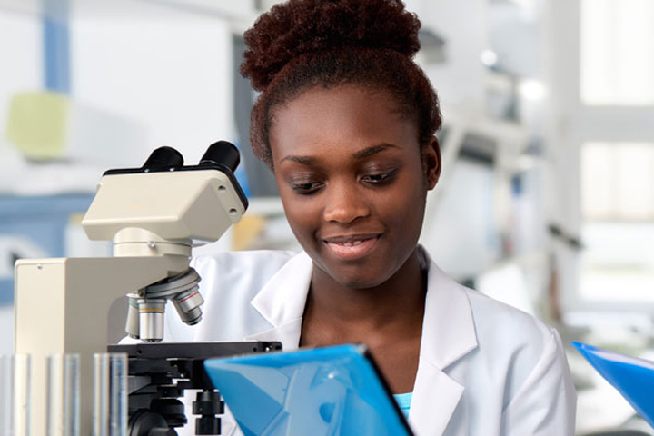 Student with brown, pinned back hair and a white lab coat preparing to analyze a sample with a microscope