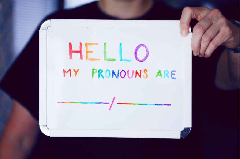A person holds up a sign reading "Hello, my pronouns are..."