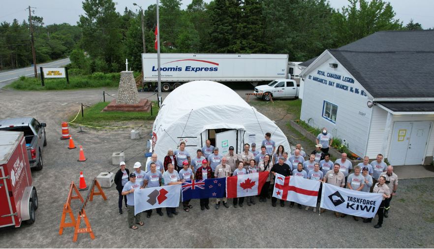 An aerial shot of a large group of people holding up a few different country flags and one for the organization Team Rubicon.