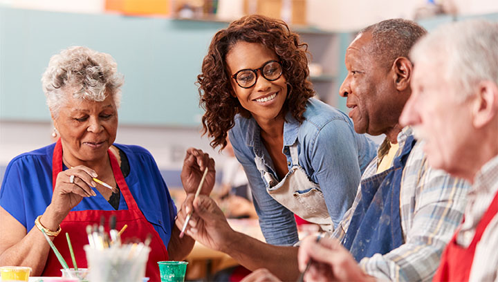 A recreational therapist in a long-term care home setting leaning over a table while seniors participate in a painting activity