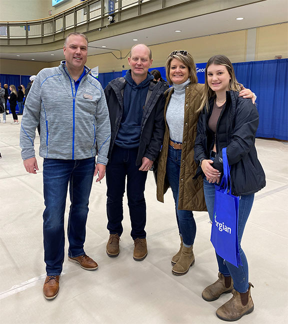 A young female (Paige Schlorff) standingn with her parents Tracey and Terry and Georgian College President and CEO Kevin Weaver in a gym. They're smiling.