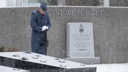 A soldier wearing blue, standing at the Georgian College Cenotaph, bowing his head in a moment of silence.