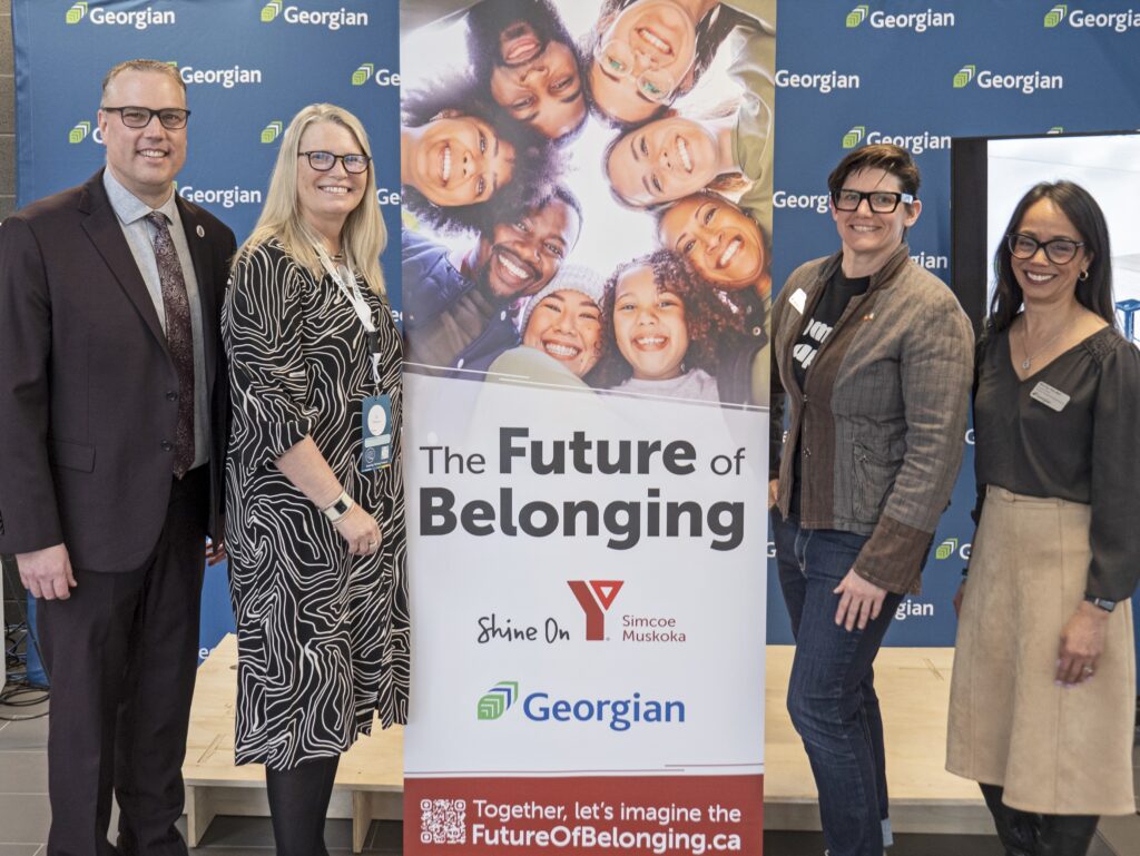 Four people stand on either side of a poster reading: The Future of Belonging. YMCA of Simcoe/Muskoka and Georgian College.